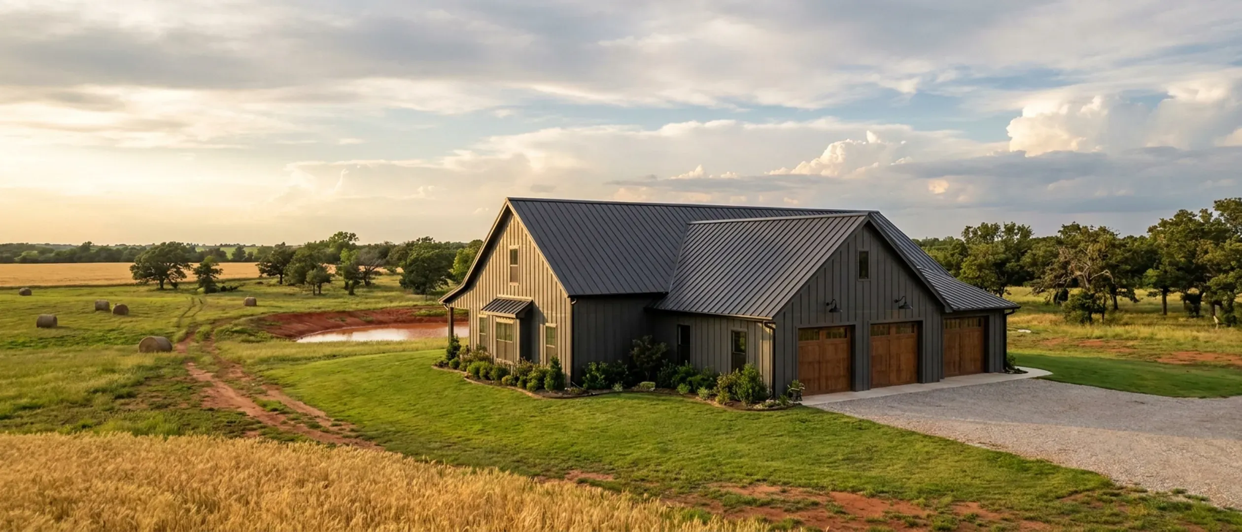 A completed barndominium viewed from a low angle showing its standing seam metal roof, vertical wall panels, gutters and exterior wall lights.