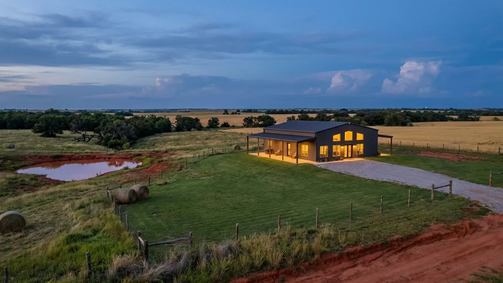 A finished barndominium at dusk with warm interior lighting glowing through its large windows.